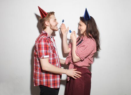 young modern cocky guy and girl have fun, laughing in party caps with pipes, isolated over whiteの写真素材