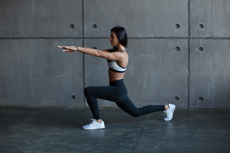 fit adult girl doing exercise lunge in gym, side viewの写真素材