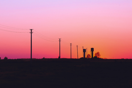 silhouettes of water towers and electricity poles on red sunset sky backgroundの写真素材