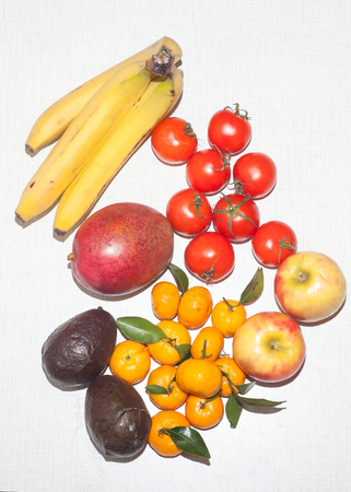 fruits - bananas, tomatoes, mango, apples, avocado, mandarin on white textured table, top view