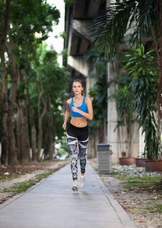 athletic caucasian woman in sportswear jogging in urban city scape under overpass, summertimeの写真素材