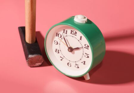 green alarm clock near hammer isolated on pink background, concept