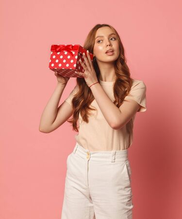 happy young woman with red gift box isolated on pink backgroundの写真素材