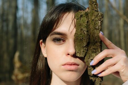 young woman close half of her face with tree bark, wild nature
