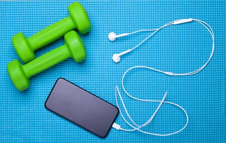 two green dummbells with smartphone with blank screen and headphones on blue exercise mat, flat layの写真素材