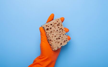 hand holding washing sponge in orange rubber glove isolated on blue backgroundの写真素材