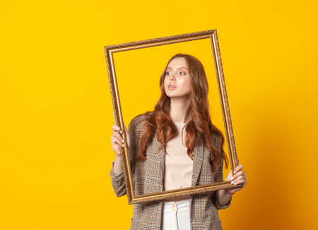 portrait of woman with empty picture art frame isolated on yellow backgroundの写真素材