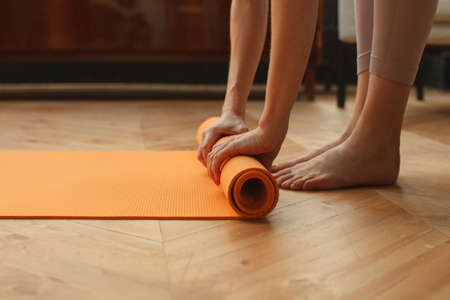 female hands unrolling yoga mat in home on parquet floor, preparing for yoga practice, detail shotの写真素材