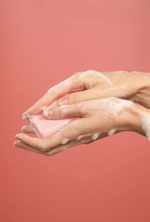 female hands using pink soap bar in foam isolated on pink background, vertical photoの写真素材