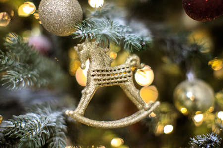 golden toy horse on christmas tree with blurred lights, close up, horizontal photo