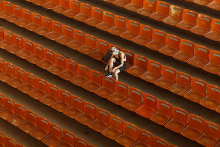 alone woman in sportswear ties shoelaces on chair in empty stadium, high angle view, horizontal photoの写真素材