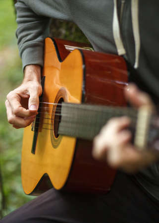 young man plays acoustic guitar on nature in forest, close up detail shot, selective focus