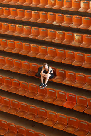 alone woman in sportswear sitting on seats in empty stadium, top view, ultra overall plan