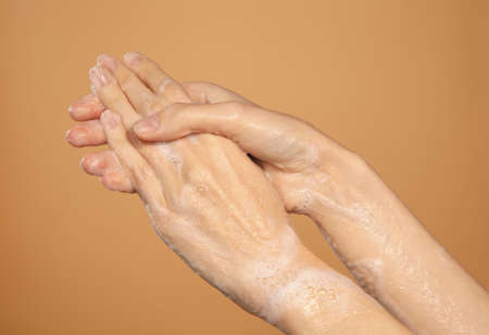 female hands washing in foam isolated on brown backgroundの写真素材