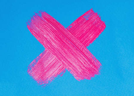 neon pink paint brush stroke cross on blue paperの写真素材