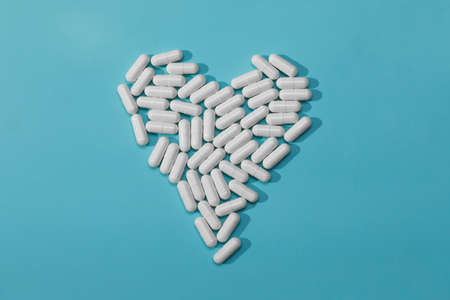 white pills in heart shape isolated on blue background, medicine concept