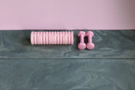 pink fitness equipment, dumbbells, self-massage roller, exercise mat on stone floor in gym, top viewの写真素材
