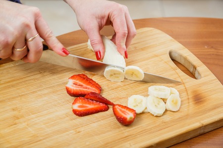 Beautiful female hands cut strawberries in the kitchenの写真素材
