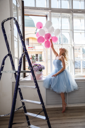 Beautiful girl blonde in dress posing with flowers in bright interiorの写真素材