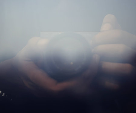 Reflection of hands holding camera at window glass