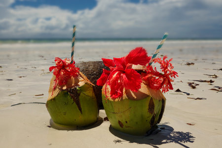 Coconut drink on the beach with red flowers in the foregroundの写真素材