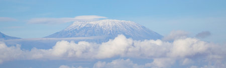 Panoramic view of snow-capped mountain peak rising above clouds on blue skyの写真素材