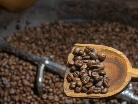 A scoop of roasted coffee beans in wooden ladle above cooling down roasted beans in the roaster.