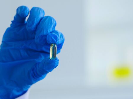 Scientists holding one tablet of medicine with 2 fingers to checking quality, color or contaminate inside the tablet. It's called visual check process.の写真素材