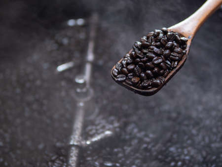 roasted coffee beans on a ladle above the cooling tray of the roaster machine. freshly roasted coffee in a wooden ladle. organic roasted coffee fresh from the roaster machine.の写真素材
