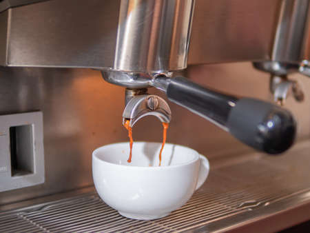 Fresh coffee pouring down from the portafilter of espresso machine into the white ceramic cup. Making hot coffee with the espresso machine.の写真素材