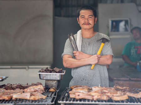 Mae Hong Son, Thailand - September 23, 2020 : Grill chef with tongs and hammer in hands at local restaurant, preparing for pounded beef and pork jerry.のeditorial素材