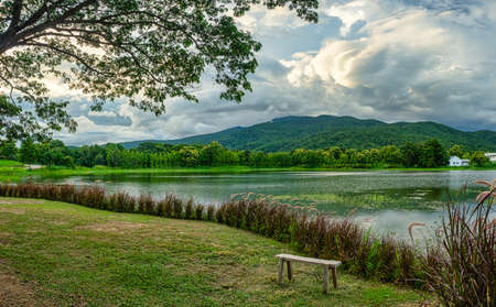 Panoramic view of the lake, forest and mountain before sunset. A bench beside the lake with a mountain and sky view. Sunset view with beauty of nature.の写真素材