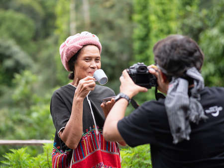 Mae Hong Son, Thailand - September 24, 2020 : Photographer shooting old Karen woman holding coffee cup and saucer.のeditorial素材