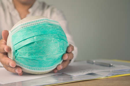 Health insurance in COVID concept. A man holds a white ball with green medical mask. Contract paper on the table. Copy space is on right side of this photo.の写真素材