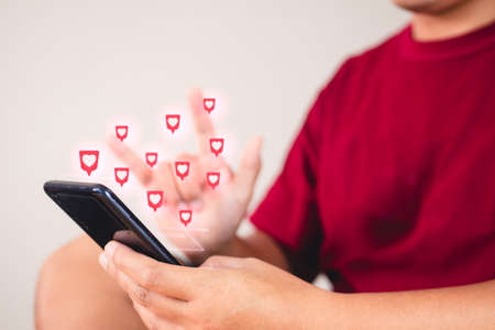 Valentine's day concept. The man uses hand sign to give love thru a smartphone. Heart shape visual effect.の写真素材