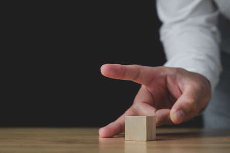 Someone uses fingers to flick a wood block. In the business, it shows a selling or cutting of some business to stop loss. Strategy Idea. This close up shot with some slightly focus.の写真素材