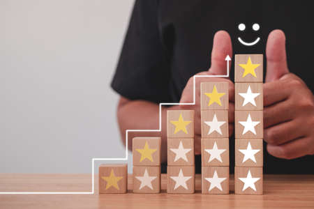 The man shows thumbs up. That is an evaluation. On the table, most wood blocks and stars are excellent job and best service for customer review. Close up shot with copy space.の写真素材