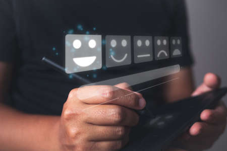 Evaluation and satisfaction concept. The man chooses a smile emotion that is an excellent review with digital pen. Medium close up shot with virtual screen.の写真素材