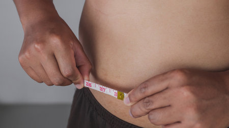 Measurement concept. The man measures a size of waistline by waist tape himself.の写真素材