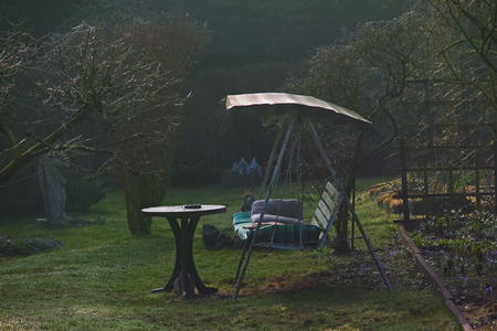 Old homemade porch swing, Hollywood swing on a meadow surrounded by plants in the garden with a fence and trees.の写真素材