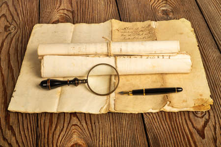 Fountain pen and magnifying glass with old sheets on wood background