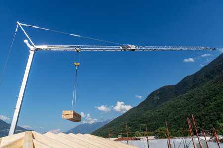 Construction crane with hanging load of wood plank on a blue skyの写真素材