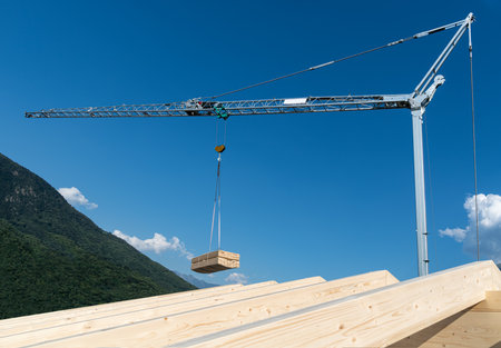 Construction crane with hanging load of wood plank on a blue skyの写真素材