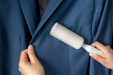 Dry cleaning and business theme: a man hand with blue suit holding a white sticky brush for cleaning clothes and furniture from dustの写真素材