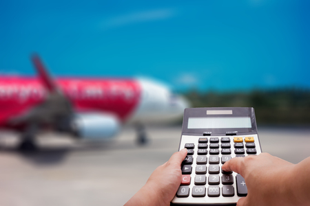 Travel cost calculation concept by calculator and airplane in backgroundの写真素材