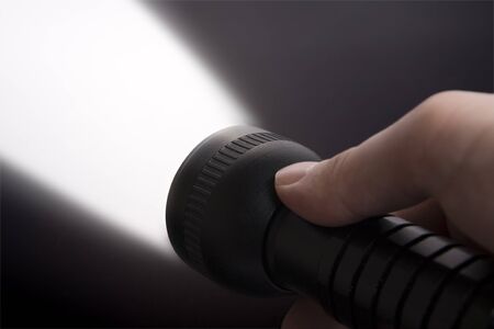 Close up of man's hand holding black  torch, with beam of light visible.の写真素材