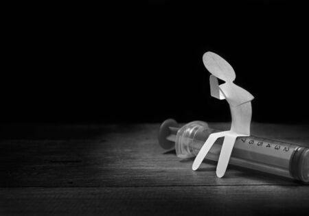 Lonely paper man sitting on syringe in darkness
