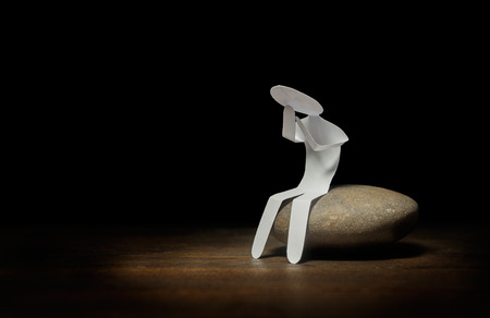 Lonely paper man sitting on stone in darknessの写真素材