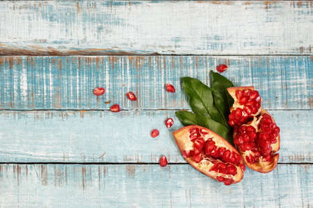 Sweet ripe sliced pomegranate on blue wood with leaves and seeds. Flat lay. Healthy eating background, text space.の写真素材