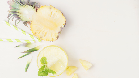 Healthy pineapple smoothie with half of pineapple and straws on bright wood. Vegetarian food background. Vegan drink concept. Detox. Text spaceの写真素材